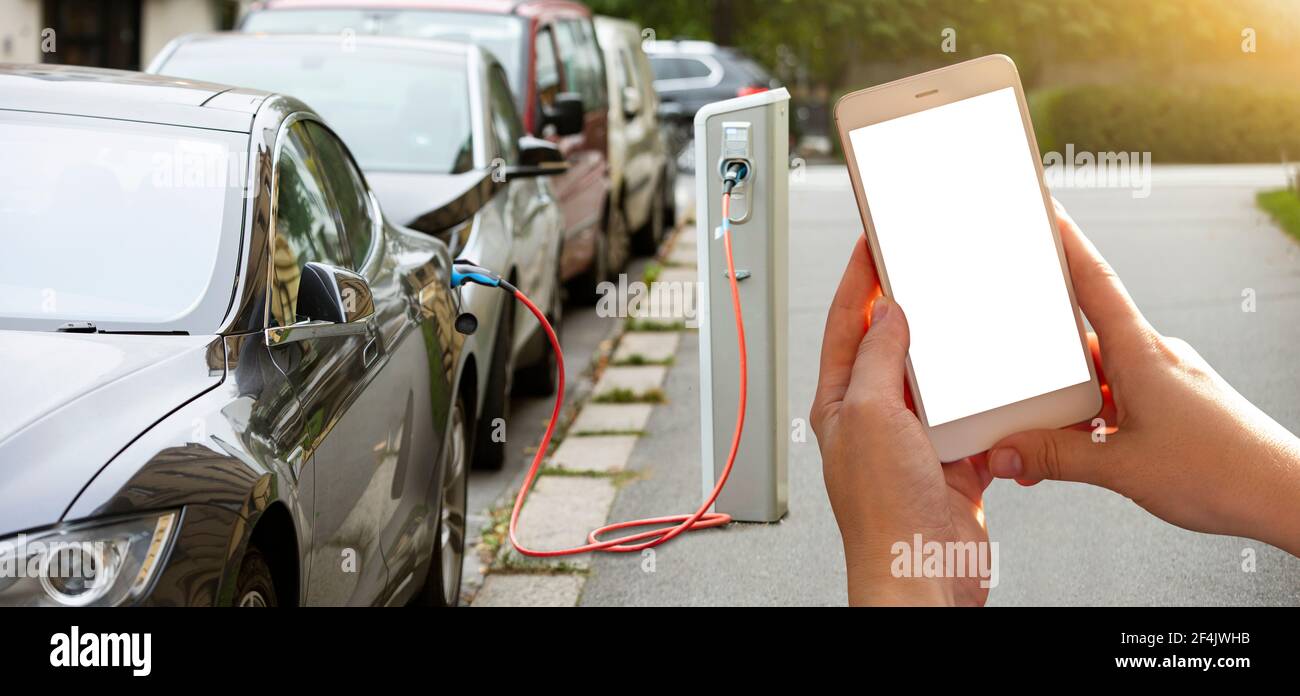 Mani con lo smartphone sullo sfondo di un'auto a noleggio presso la stazione di ricarica per i veicoli elettrici. Condivisione dell'auto. Foto Stock