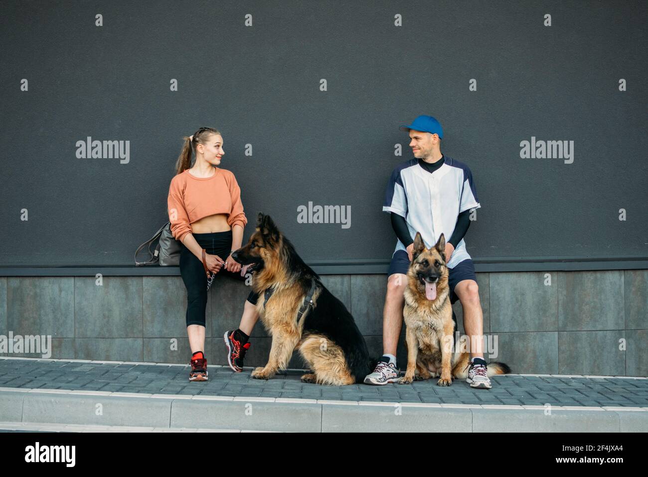 PET Love, addestramento del cane, migliori razze di cane per la famiglia. Giovani coppie sportive che camminano con due cani tedeschi Shepherd all'aperto nel parco estivo Foto Stock