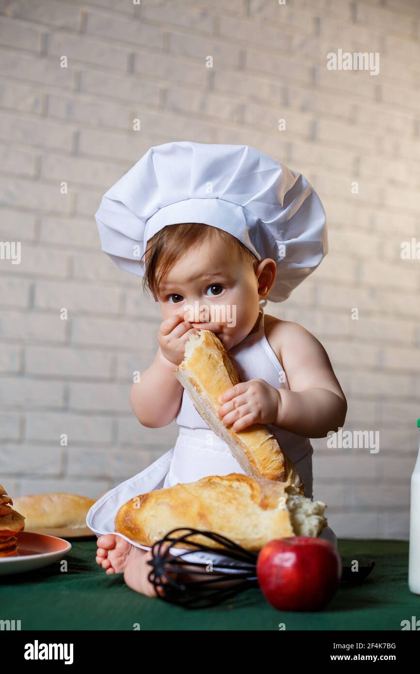 Ragazzino vestito da cuoco in cucina. Bel bambino vestito in un grembiule  che mangia pane Foto stock - Alamy