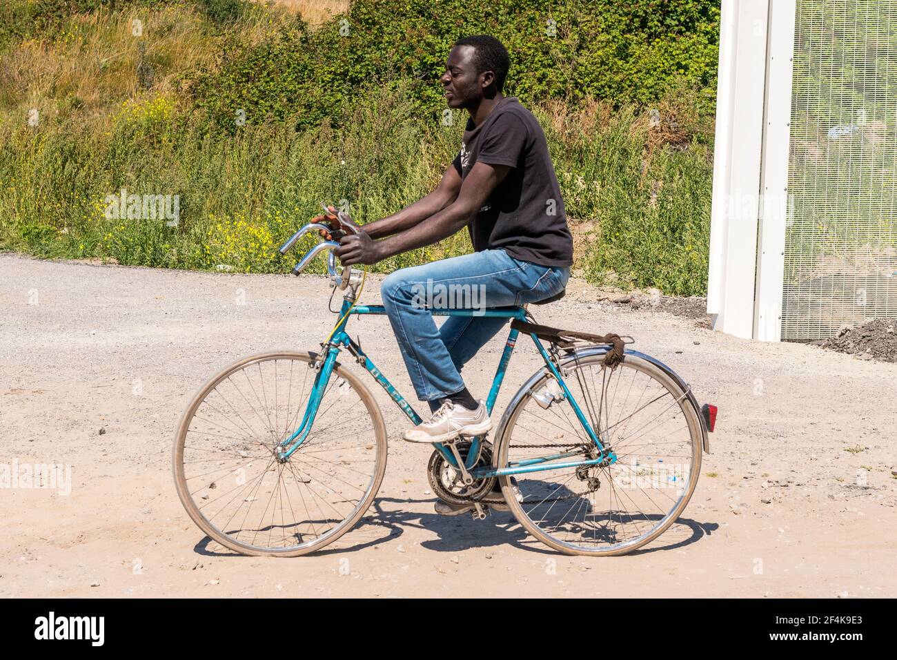 Calais, Francia. Un immigrato illegale dal continente africano imparando a guidare una bicicletta, mentre pianifica il suo viaggio verso l'Oceano Atlantico / il Chanel verso il Regno Unito / Inghilterra. Lui e molti dei suoi colleghi rifugiati / migranti vivono in cattive condizioni all'interno della giungla, poiché le misure per impedire di viaggiare nel Regno Unito, rendono una transizione sempre più difficile. Foto Stock