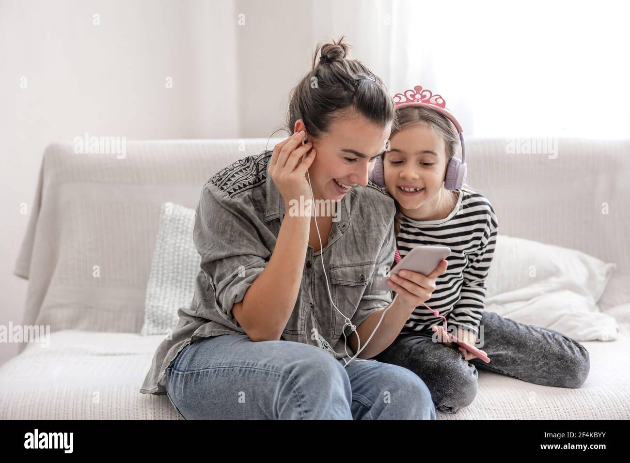 Madre e figlia allegre riposano a casa, ascoltando musica con le cuffie. Il concetto di una famiglia felice e relazioni amichevoli. Foto Stock