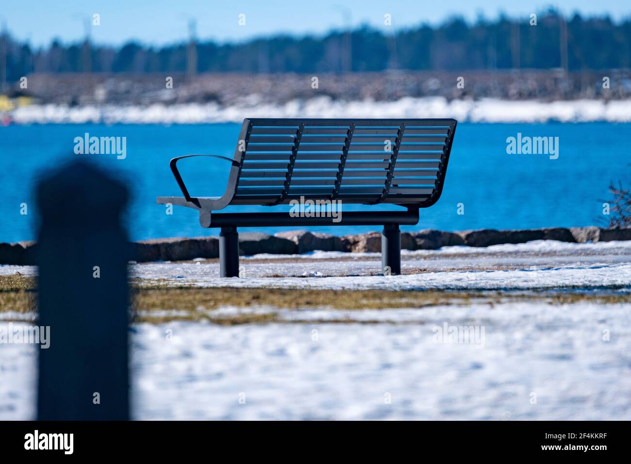 Helsinki / Finlandia - 22 MARZO 2021: Un closeup di una panchina metallica del parco proprio accanto al lungomare in una soleggiata giornata di primavera. Foto Stock