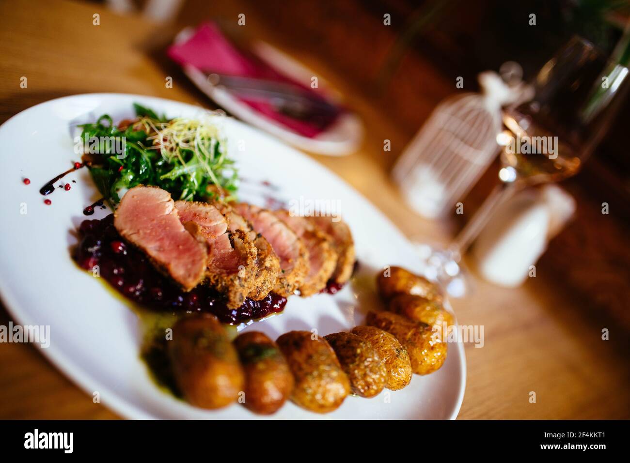 Filetto di maiale con patate grenaille e insalata fresca in ambiente ristorante di lusso, posate e bicchiere di vino Foto Stock