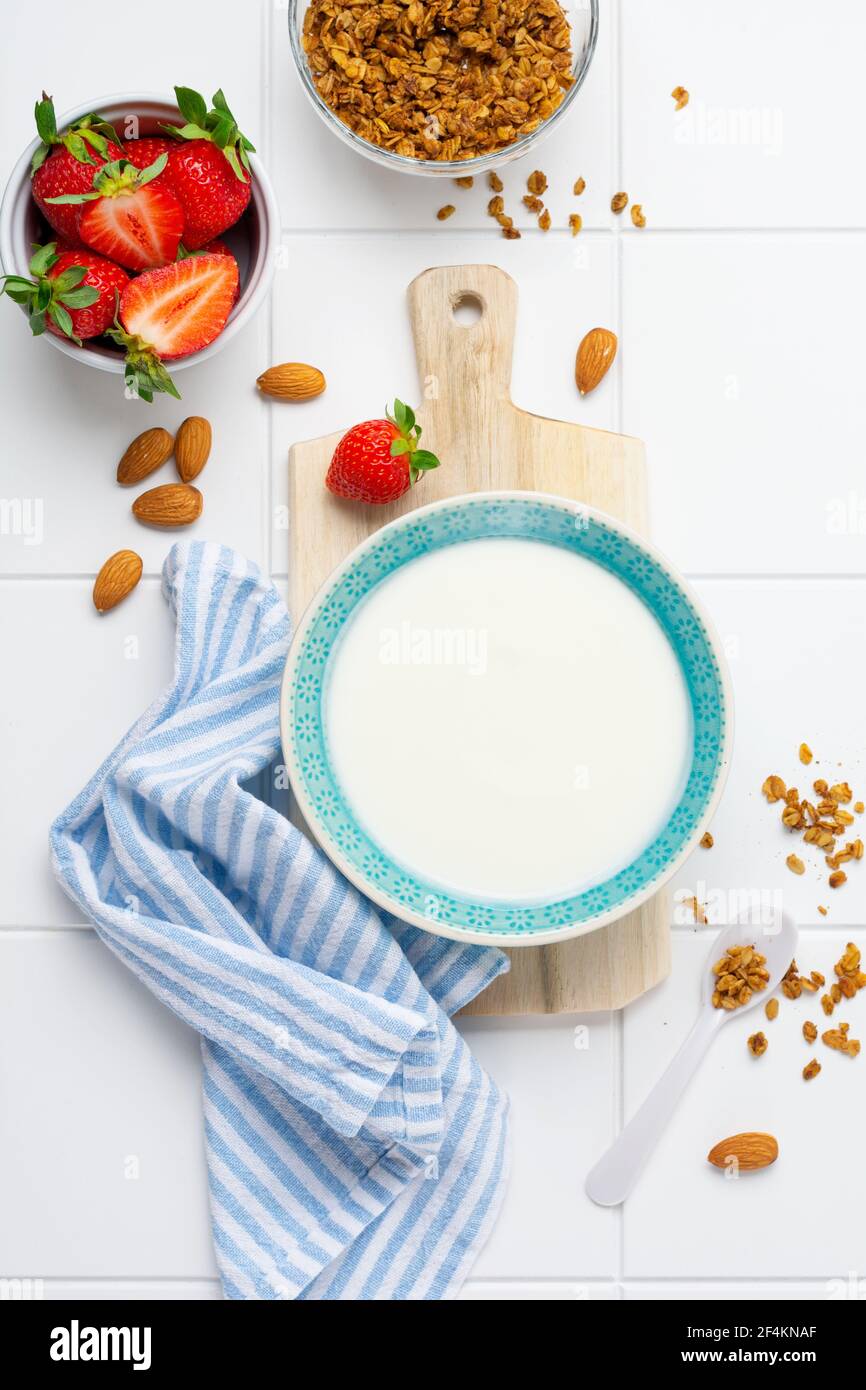 Yogurt greco in ciotola bianca con ingredienti per preparare la colazione a base di muesli e fragole fresche su tavola bianca. Vista dall'alto Foto Stock