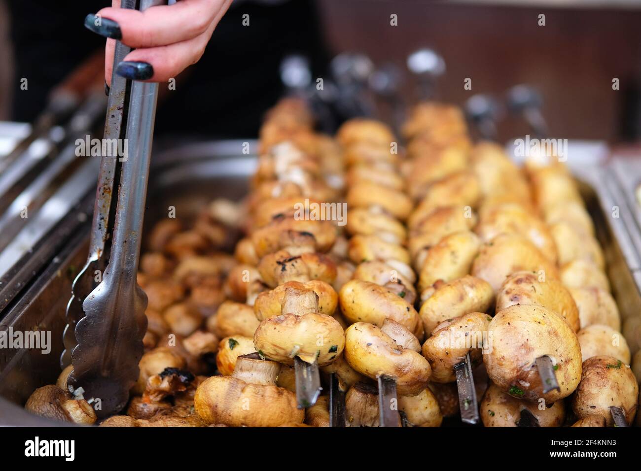 Funghi alla griglia in cucina aperta festival alimentare evento. Street food e cucina all'aperto. Mano di donna con i denti. Foto Stock