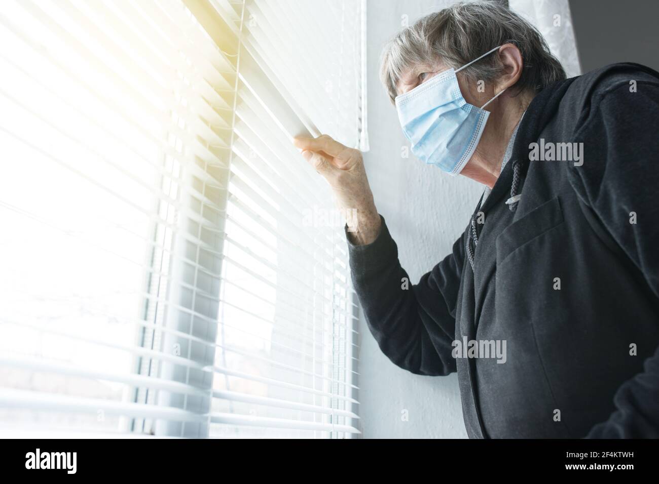 Donna anziana a casa su auto-isolamento, in maschera medica vicino alla finestra guardando outsid.e Foto Stock