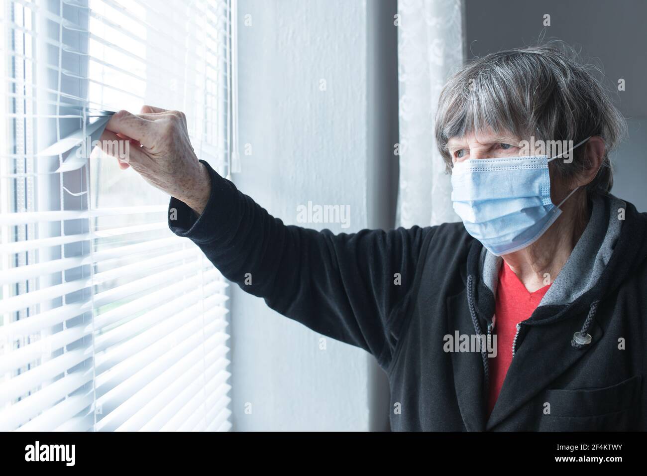 Vecchia signora con maschera medica a casa durante la quarantena lokk fuori la finestra. Foto Stock