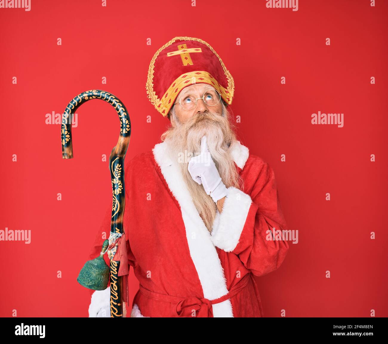 Uomo anziano con capelli grigi e barba lunga il costume tradizionale di san nicola si concentrò sul dubbio con il dito sul mento e guardare Foto Stock