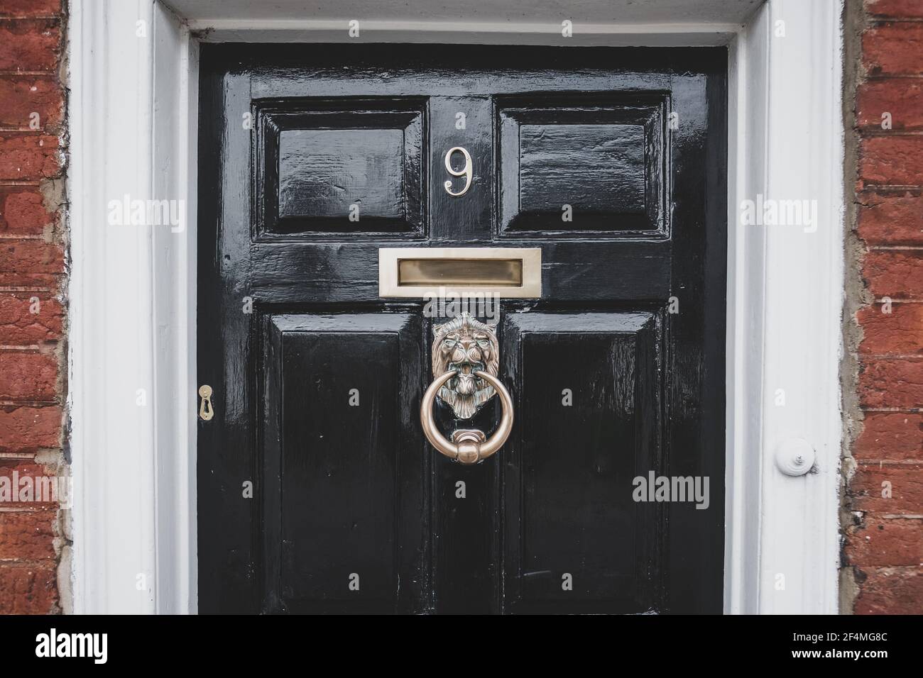 Antica porta in legno ornata vista all'ingresso di una casa. Le caratteristiche in ottone e un battitalcagno ornato sono chiaramente visibili insieme alla vernice lucida. Foto Stock