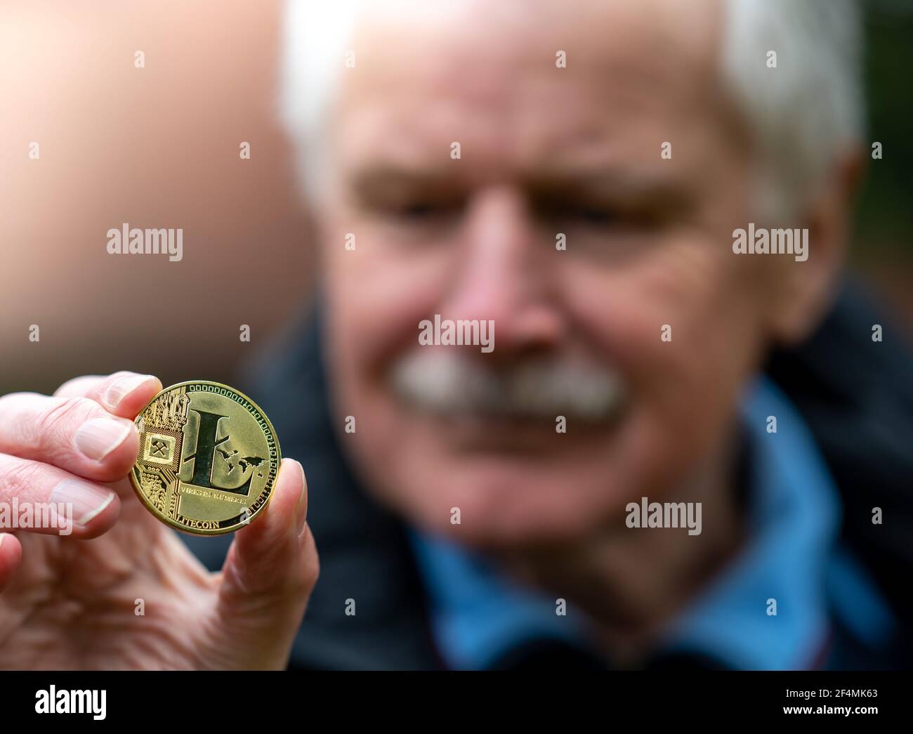 Simbolo di Litecoin come investimento del piano di pensionamento. Anziano che tiene un litecoin. Foto Stock