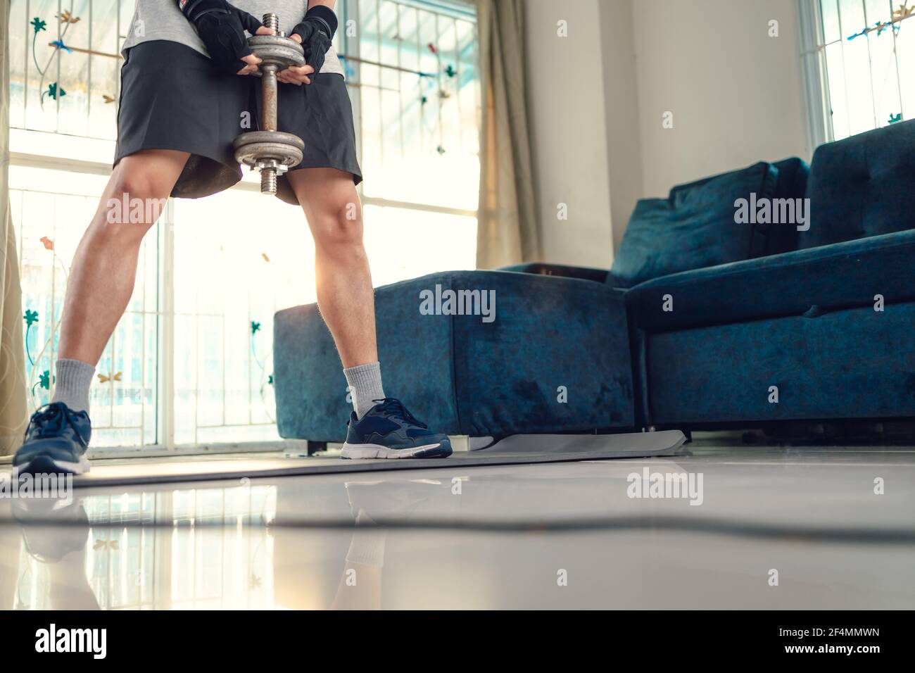 Giovane uomo che fa esercizi di squat con manubri sul tappetino yoga in soggiorno a casa. Concetto di fitness, allenamento e traning a casa. Foto Stock