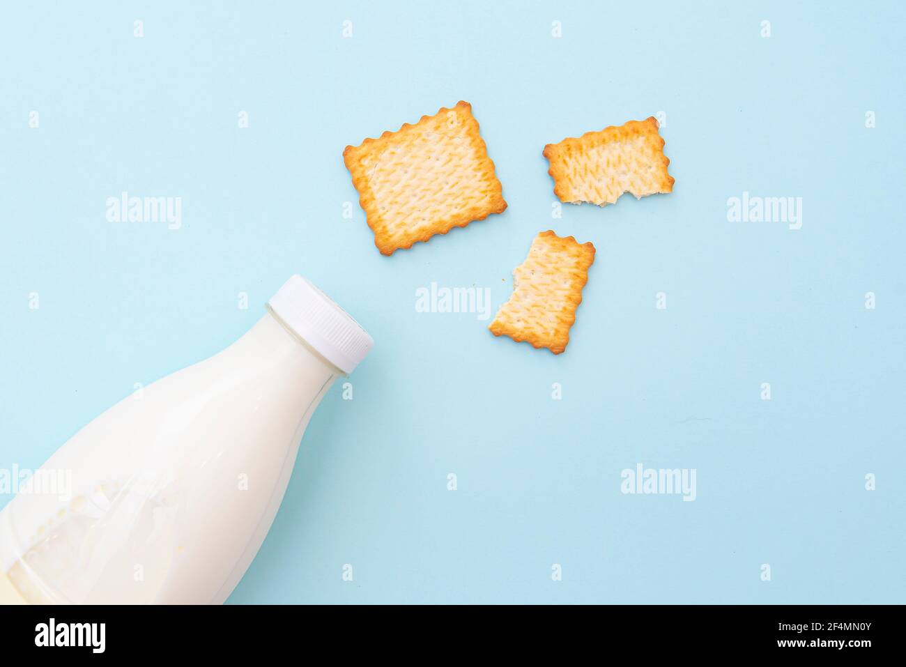 Biscotti secchi rotti e bottiglia di latte su sfondo blu, vista dall'alto, disposizione. Immagine del concetto di cibo e colazione Foto Stock