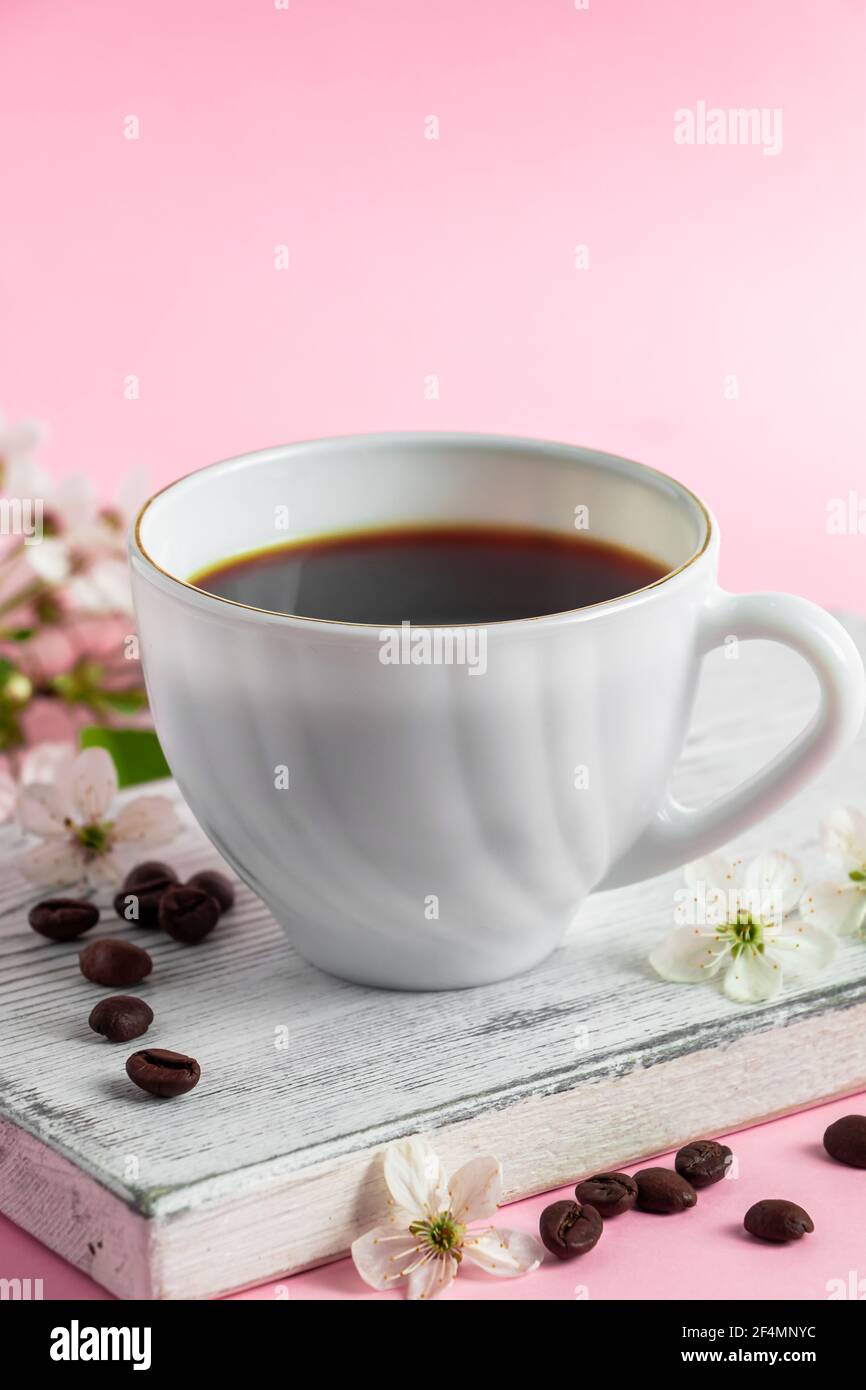 Tazza di caffè espresso forte e delicati fiori primaverili su sfondo rosa. Concetto di primavera e buon mattino. Foto Stock