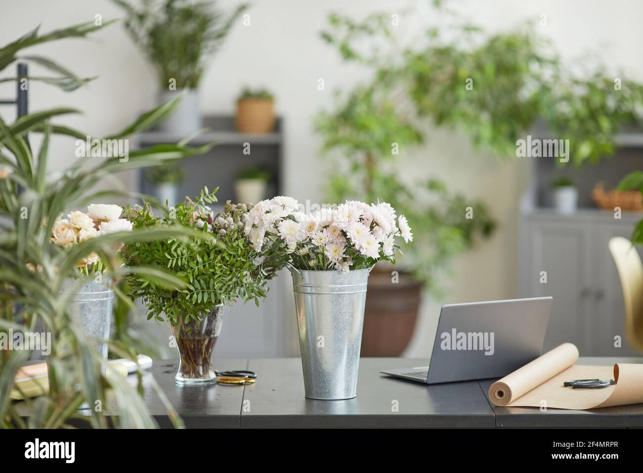 Immagine di sfondo di composizioni floreali minime in secchi rustici in metallo su tavolo in laboratorio fioristi verdi, spazio copia Foto Stock