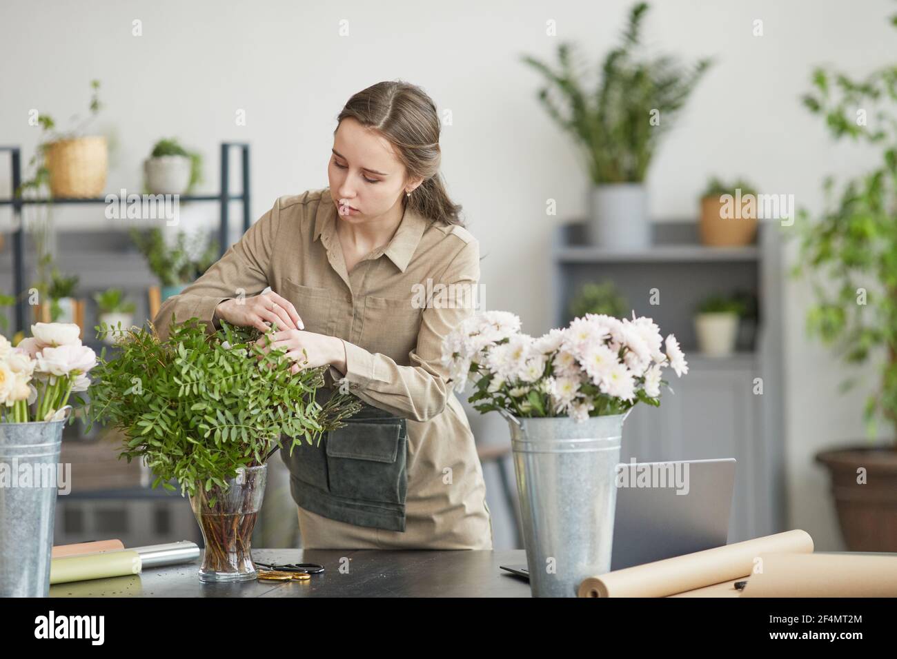 Ritratto di giovane donna che organizza composizioni floreali in laboratorio fioristi verdi, copy space Foto Stock