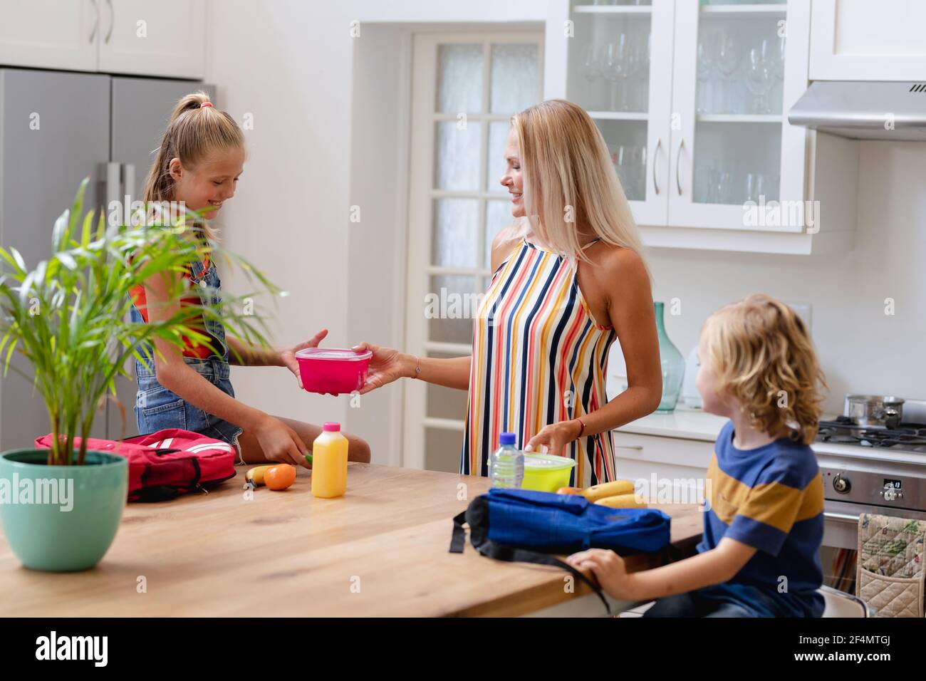 Sorridente madre caucasica con figlio e figlia che preparano pranzi al sacco e borse da scuola in cucina Foto Stock