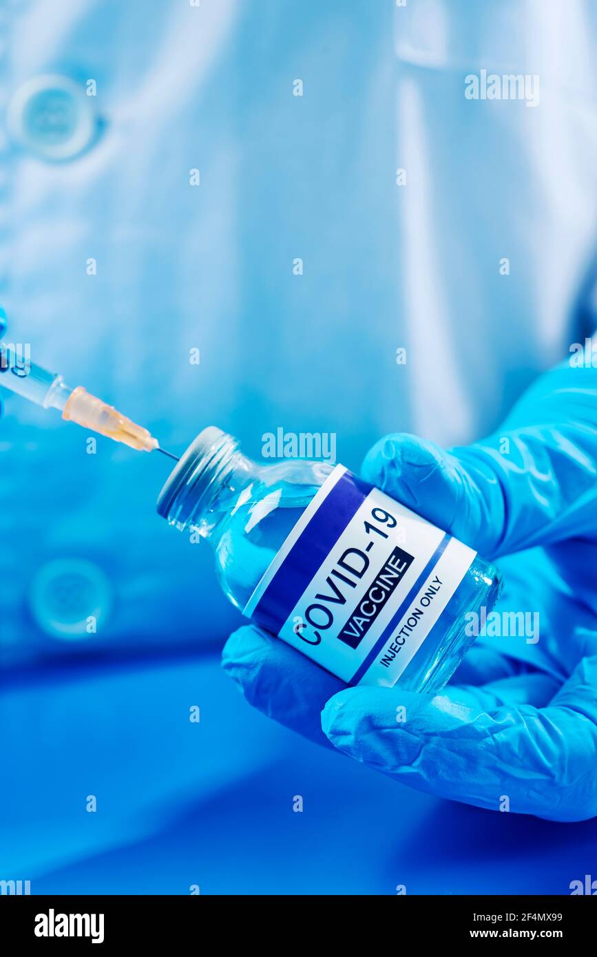 chiusura di un operatore sanitario o di laboratorio, indossando guanti chirurgici blu, riempiendo una siringa da un flaconcino di un vaccino simulato covid-19 Foto Stock
