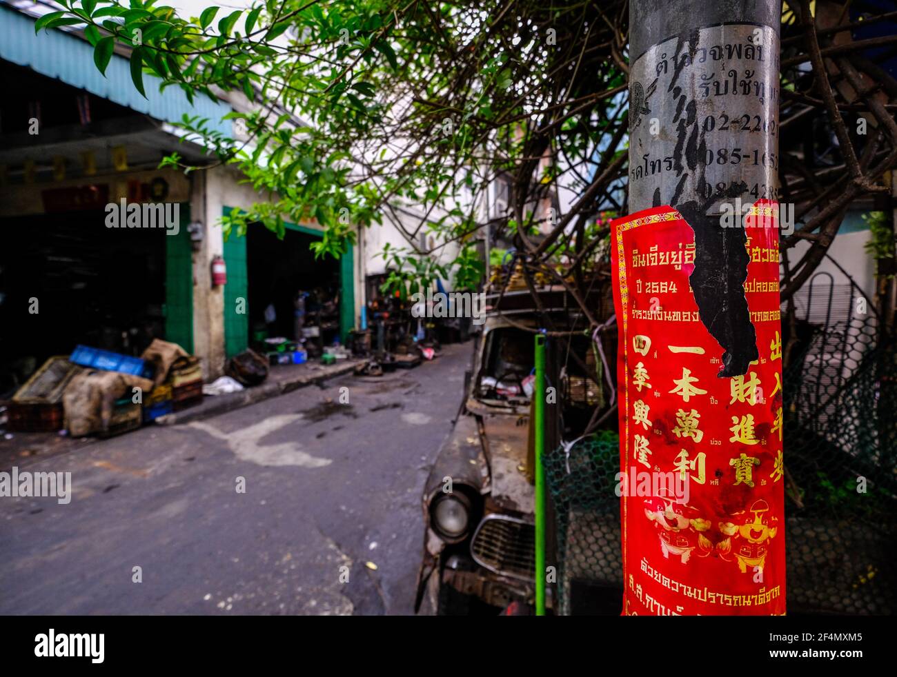 Un lampione coperto da un poster rosso con scritta in oro cinese si trova all'ingresso di un piccolo vicolo posteriore a Talat noi, Bangkok, Thailandia Foto Stock