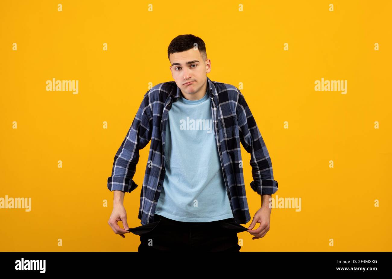 Un giovane ragazzo sconvolto che mostra tasche vuote sullo sfondo arancione dello studio Foto Stock