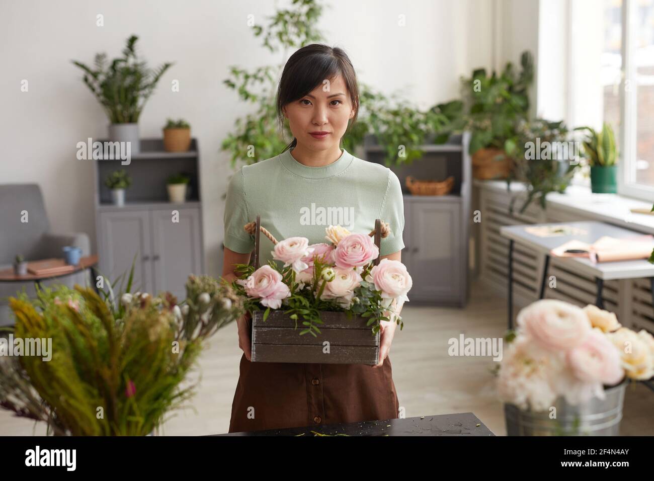 Vita in su ritratto di giovane donna asiatica che tiene i fiori e guardando la macchina fotografica mentre posa in officina fioristi, copy spazio Foto Stock