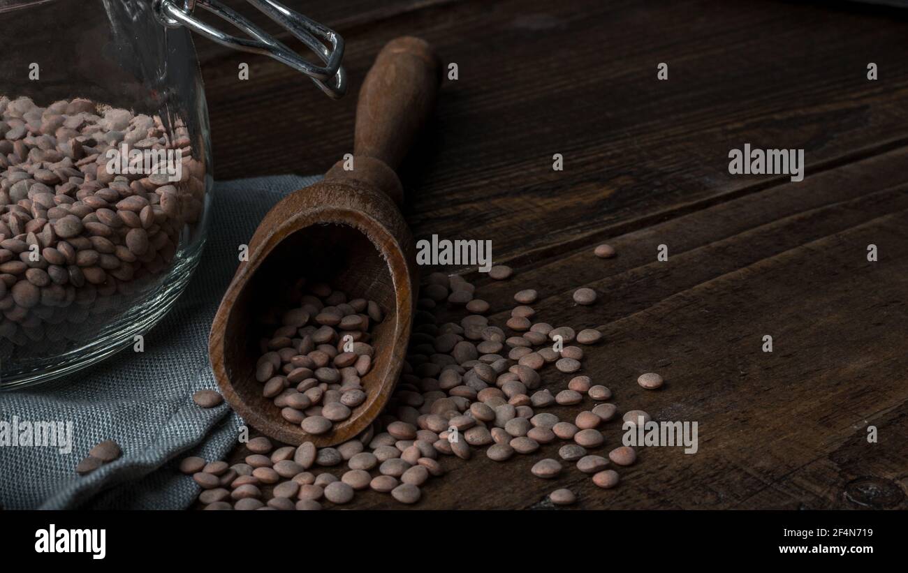 Colpo di closeup di un mucchio di lenticchie, una paletta di legno e un vaso trasparente su una superficie di legno Foto Stock