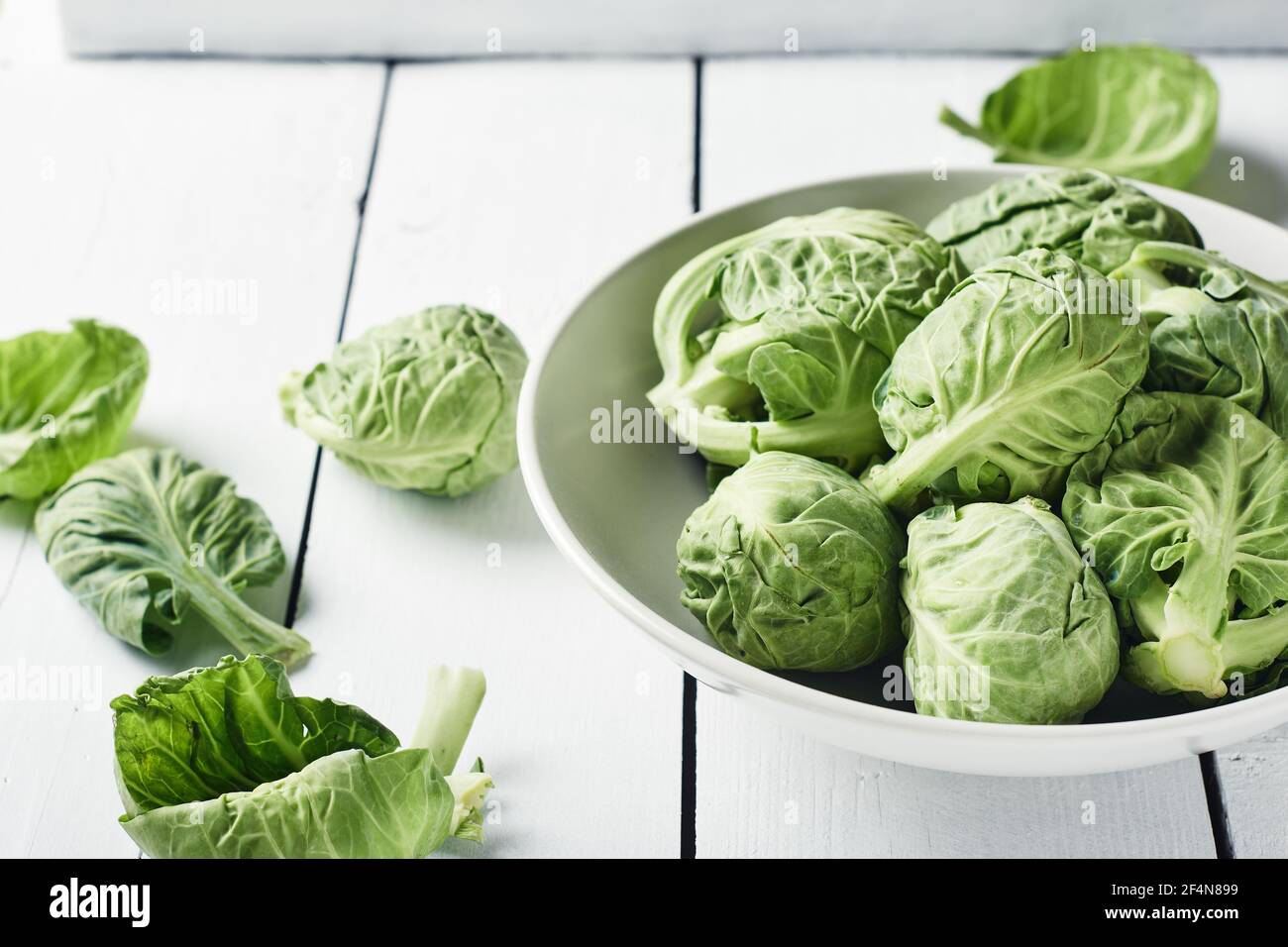 germogli di bruxelles freschi e crudi in una ciotola su un tavolo di legno bianco. Foto Stock