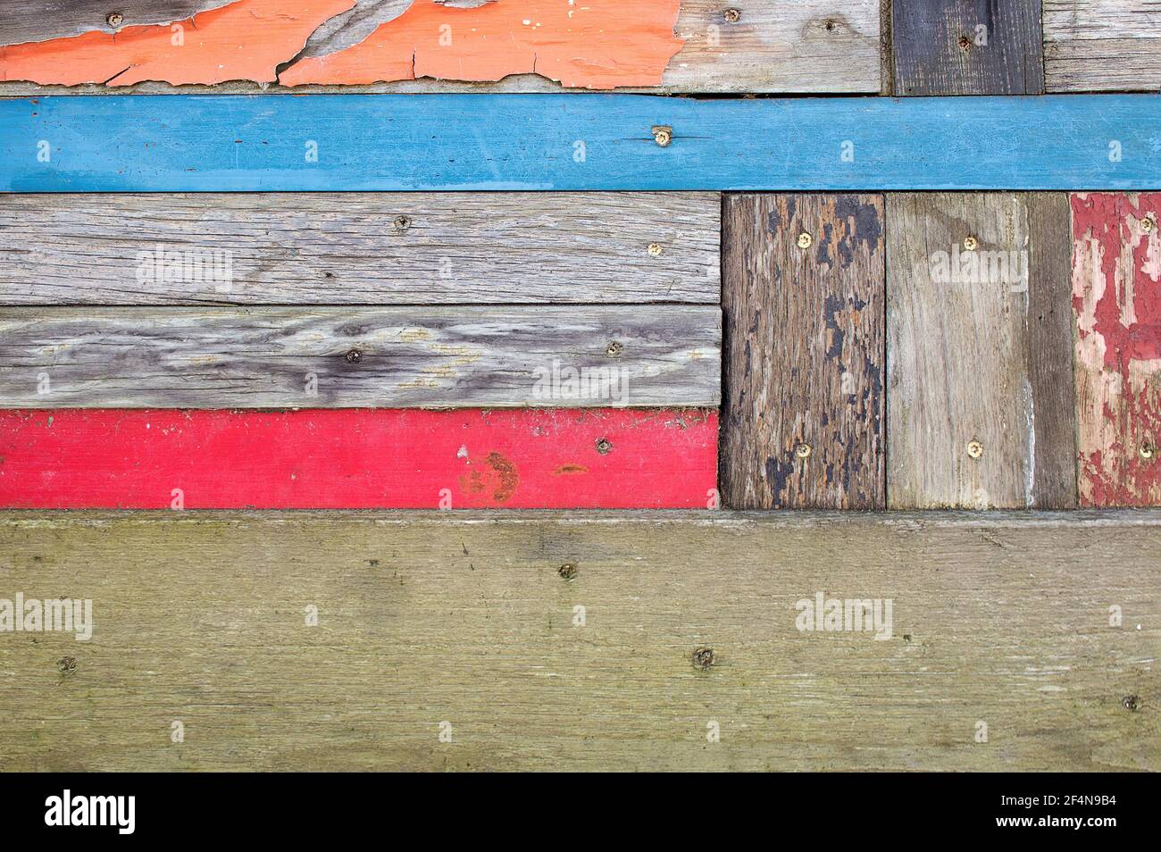 Vernice arancio, rosso e blu sbiadita su legno grigio resistente alle intemperie Foto Stock