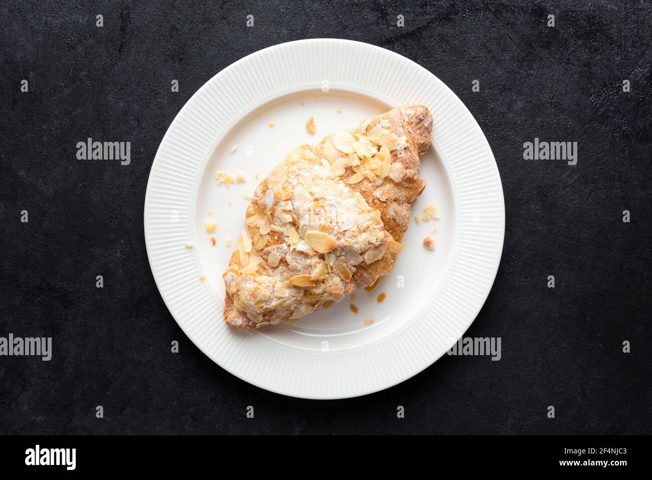 Croissant alle mandorle dolci su piastra bianca, fondo in cemento nero, vista dall'alto. Pasticceria francese Foto Stock