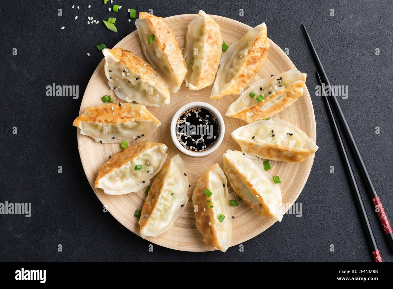 Gnocchi cinesi fritti Gyoza o Jiaozi su piatto di bambù servito con salsa di soia, vista dall'alto, fondo nero di cemento Foto Stock