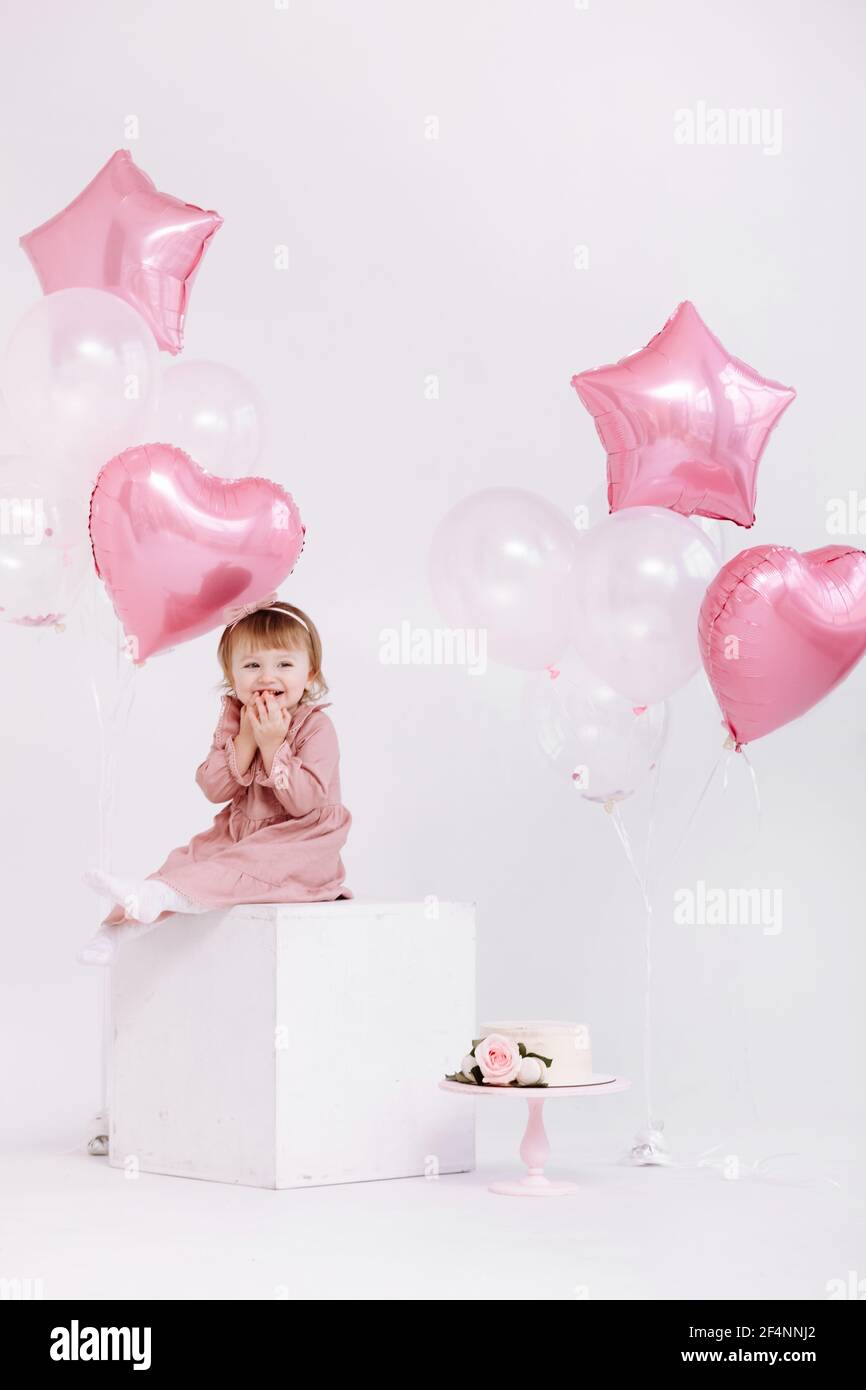 buon compleanno bambina di 2 anni in abito rosa. torta bianca con candele e  rose. Decorazioni di compleanno con palloncini bianchi e rosa e Foto stock  - Alamy