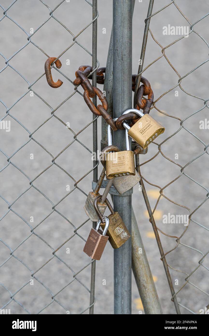 Lucchetti multipli con una spessa catena arrugginita su recinzione metallica proibendo l'ingresso alla proprietà dietro Foto Stock