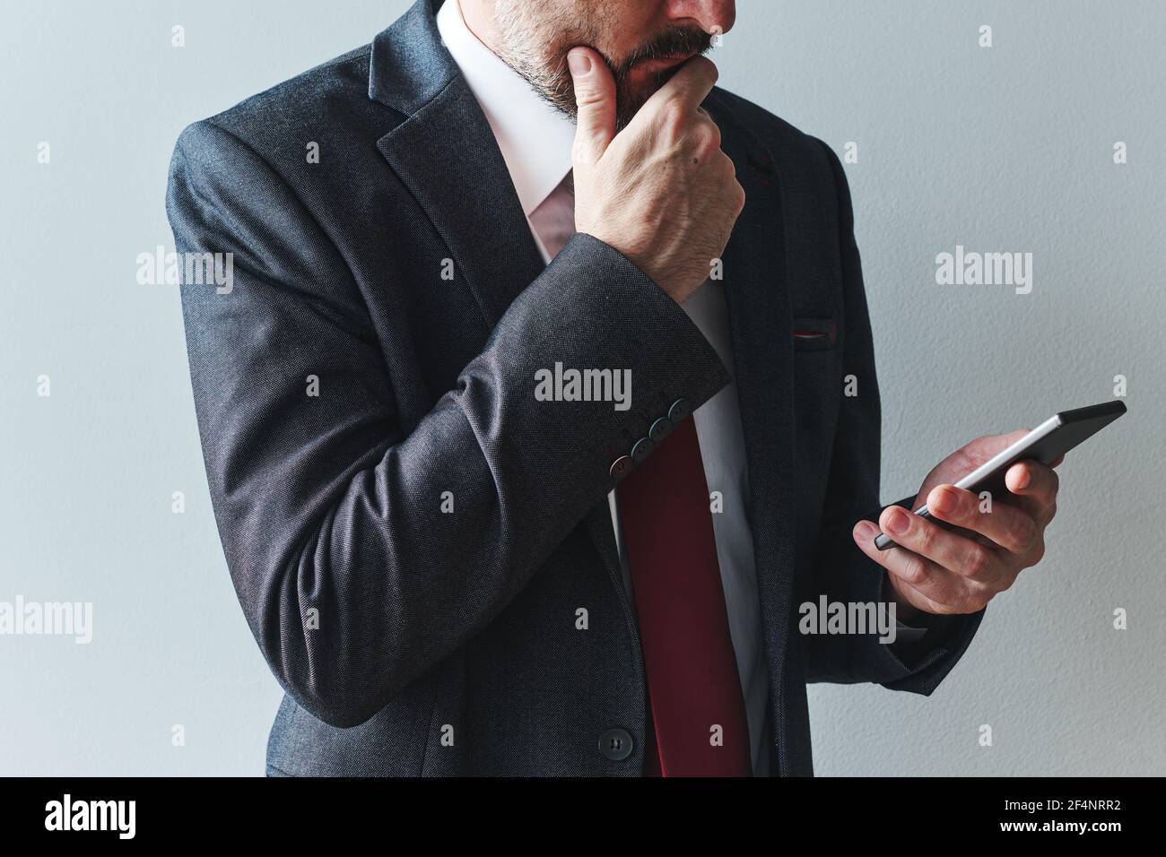 Imprenditore afflitto che utilizza lo smartphone mobile, leggendo un messaggio di posta elettronica o di testo. Elegante uomo d'affari in tuta utilizzando la tecnologia di comunicazione. Foto Stock