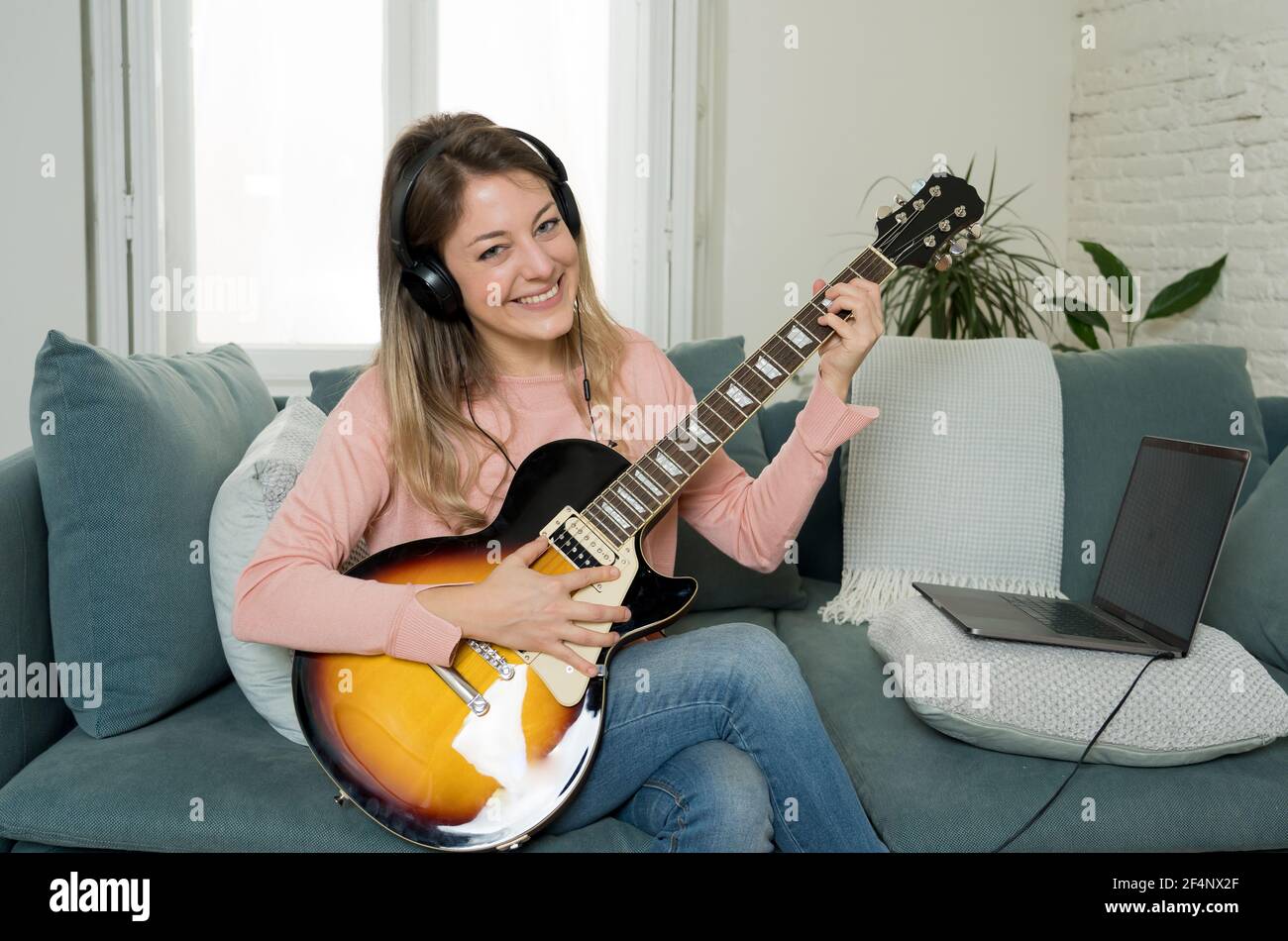 Donna che suona la chitarra elettrica con un laptop in una lezione di  musica online. Donna