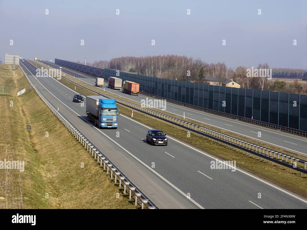 Veicoli che viaggiano in autostrada. Barriere fonoassorbenti visibili che separano l'autostrada dall'area residenziale. Foto Stock