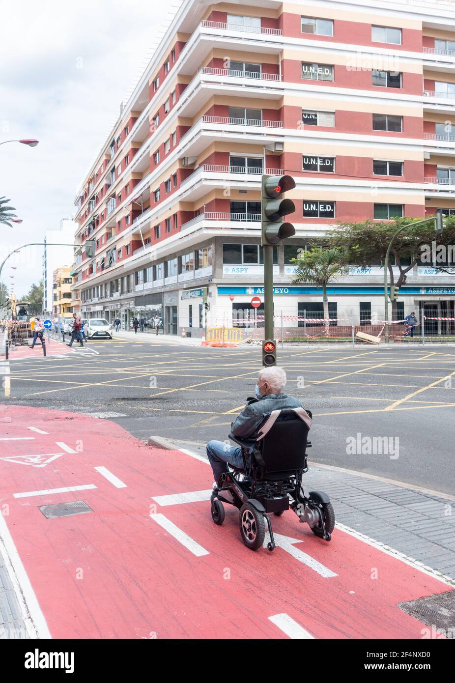 Uomo anziano in sedia a rotelle in attesa al semaforo in bicicletta Corsia in Spagna Foto Stock