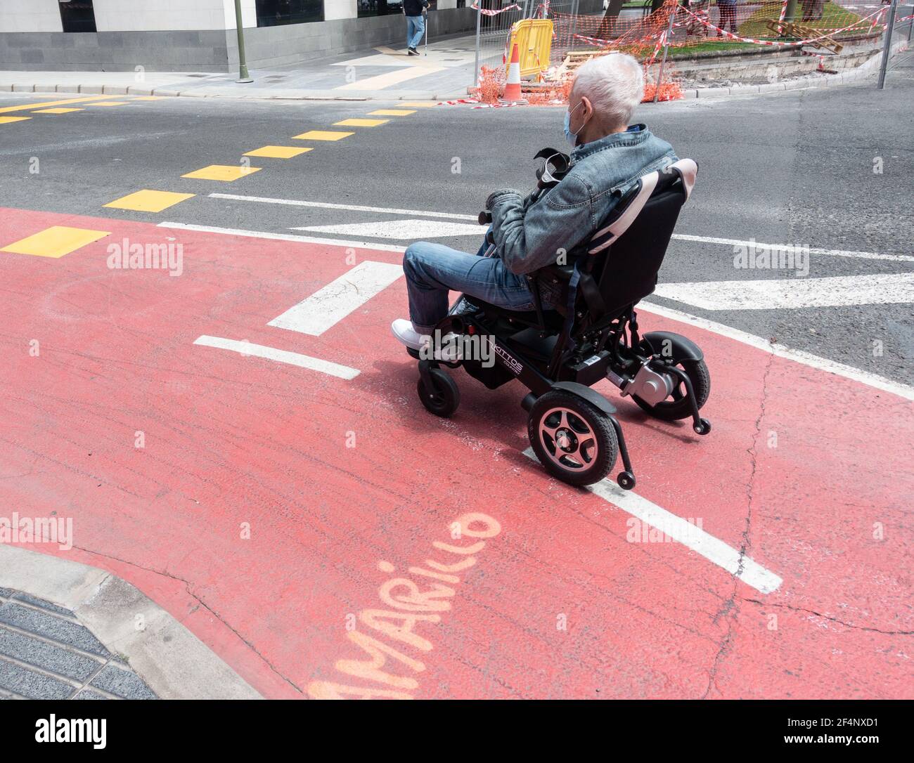 Uomo anziano in sedia a rotelle in attesa al semaforo in bicicletta Corsia in Spagna Foto Stock