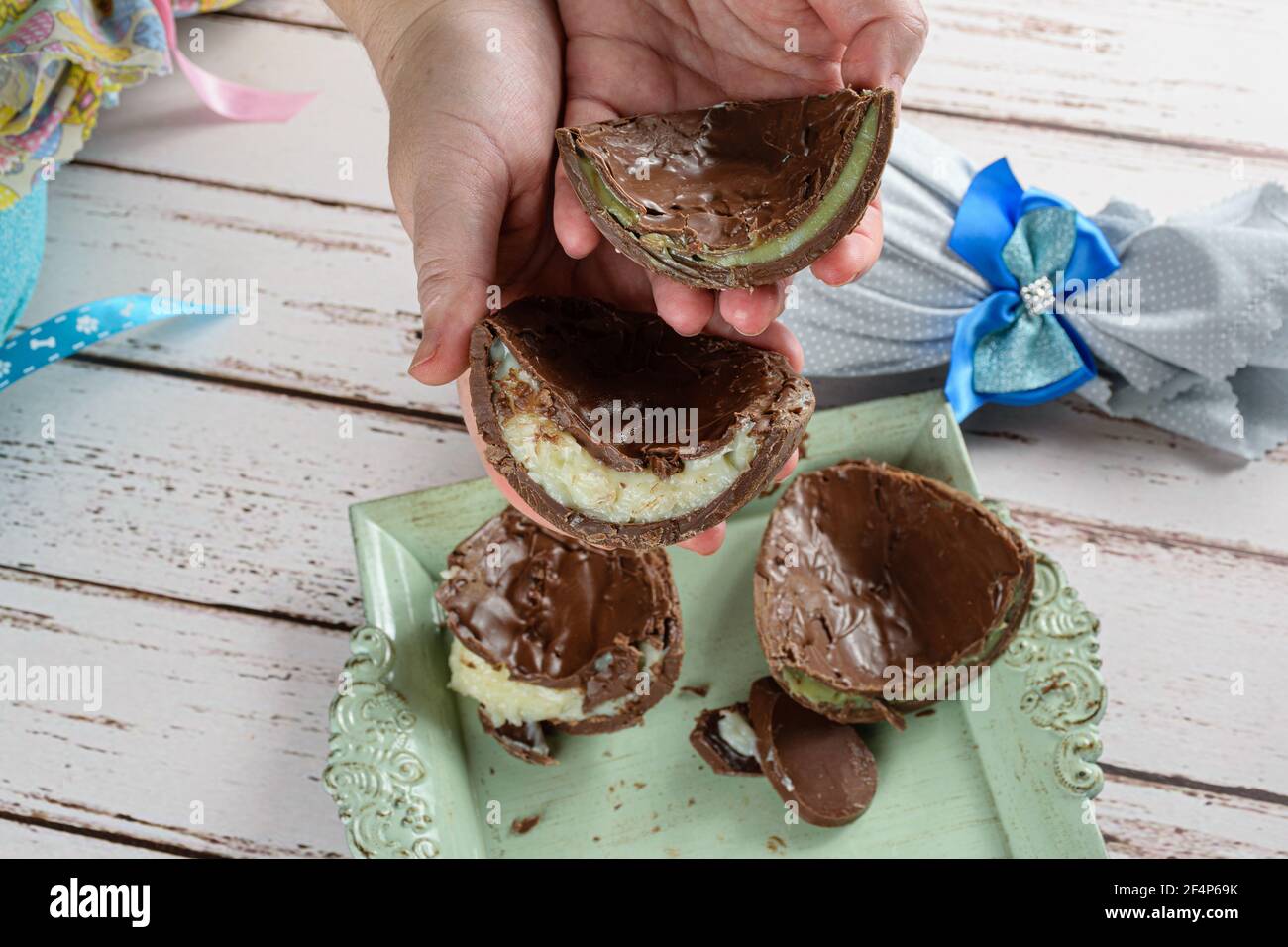 Donna che tiene due metà di uova di Pasqua di cioccolato farcite con brigadeiro bianco e brigadeiro con pistacchi. Sullo sfondo, uovo di Pasqua con una r Foto Stock