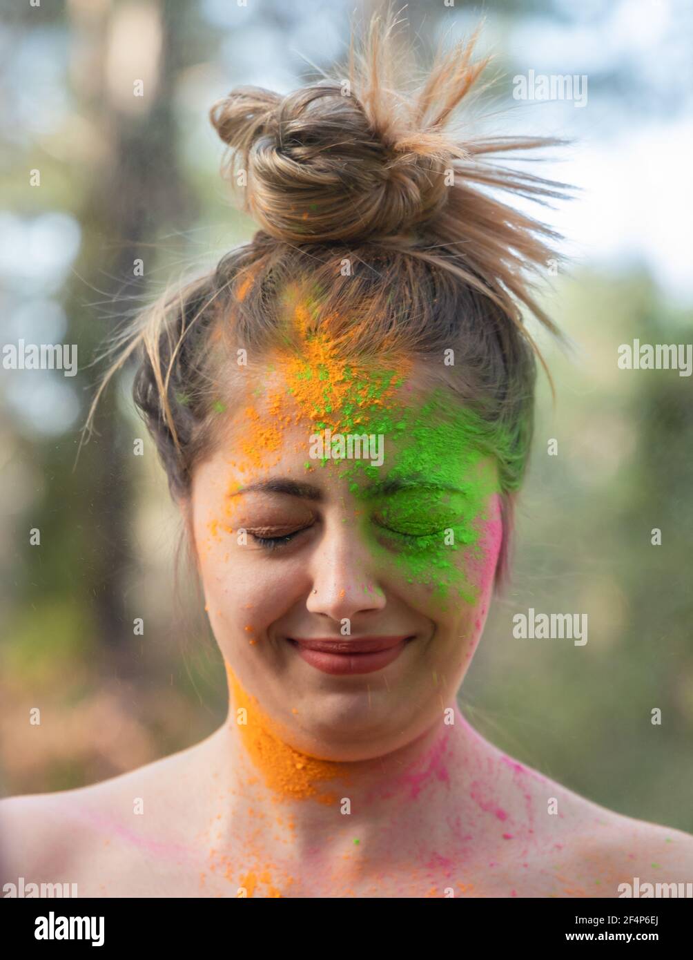 Giovane donna attraente al festival di colori Holi di pitture nel parco. Divertirsi all'aperto. Polvere multicolore colora il viso. Primo piano verticale. Foto Stock