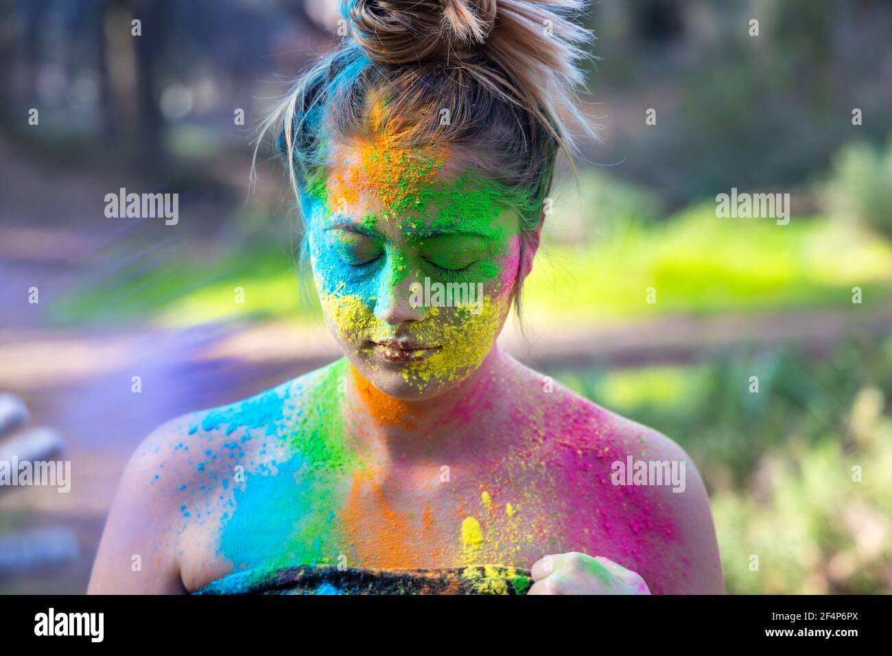 Giovane donna attraente al festival di colori Holi di pitture nel parco. Divertirsi all'aperto. Polvere multicolore colora il viso. Primo piano verticale. Foto Stock