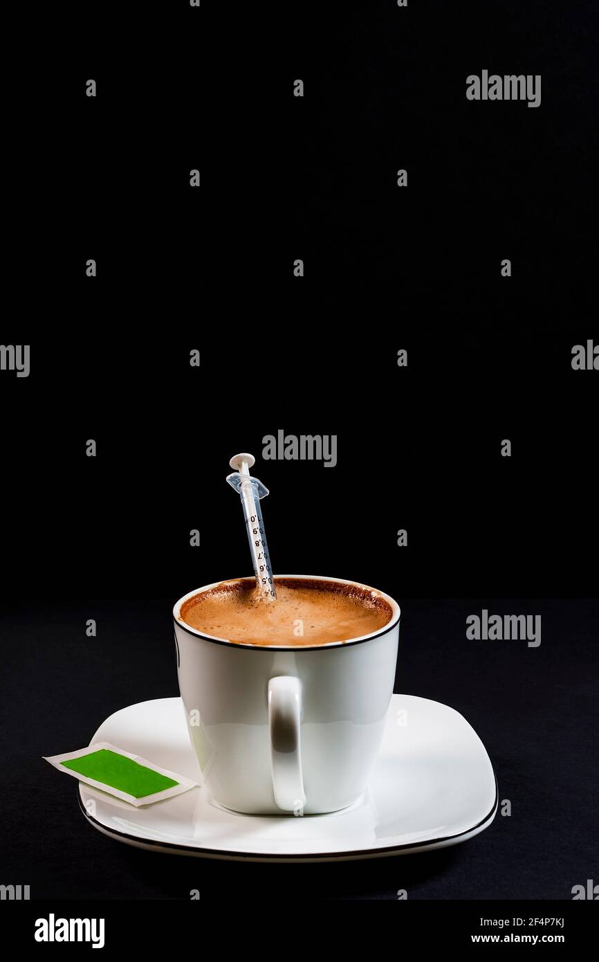 Caffè con latte in tazza di porcellana con siringa all'interno del Coffee.questa è una foto in formato ritratto scattata contro un nero sfondo sotto lig artificiale Foto Stock