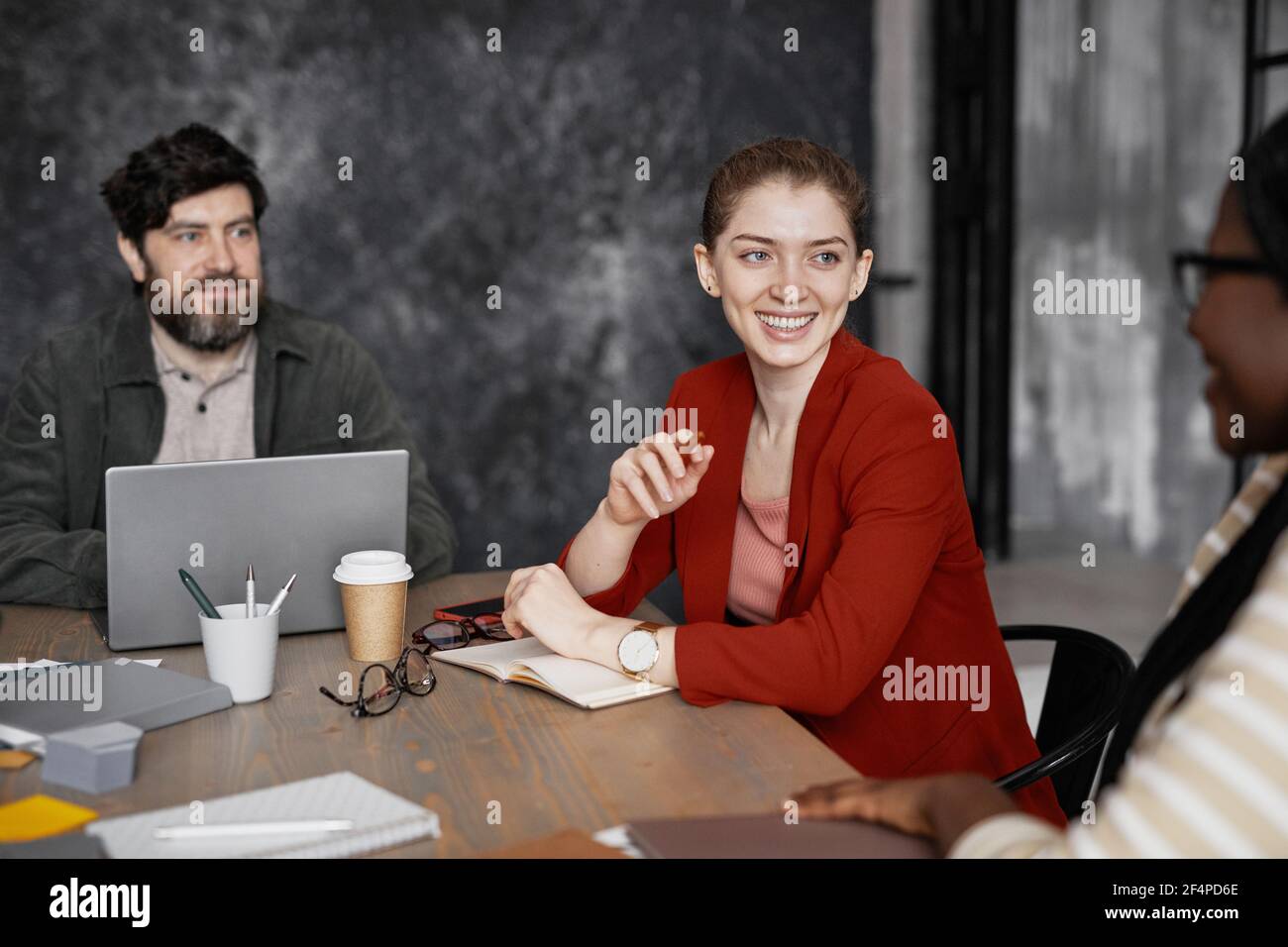 Ritratto di giovane donna d'affari sorridente che indossa giacca rossa durante l'incontro con i colleghi in ufficio, copy space Foto Stock