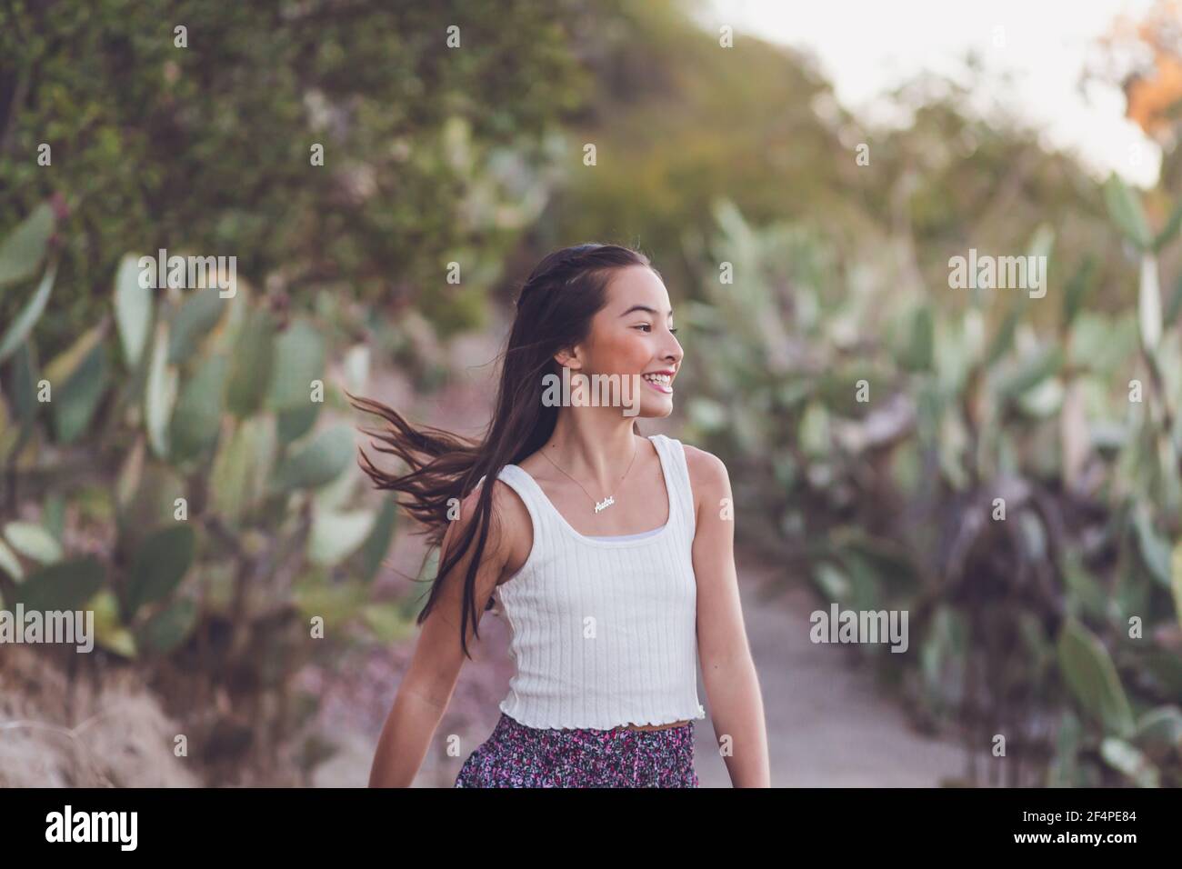 Misto razza ragazza che cammina su un percorso cactus con i suoi lunghi capelli volare. Foto Stock