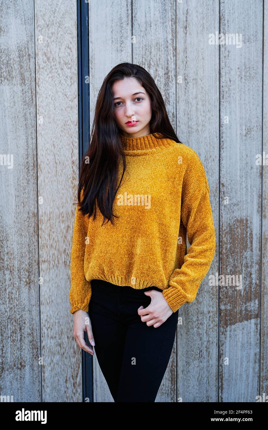 Foto verticale di un Ritratto di una giovane bruna con labbra dipinte e in un maglione giallo e nero jeans su sfondo di legno Foto Stock