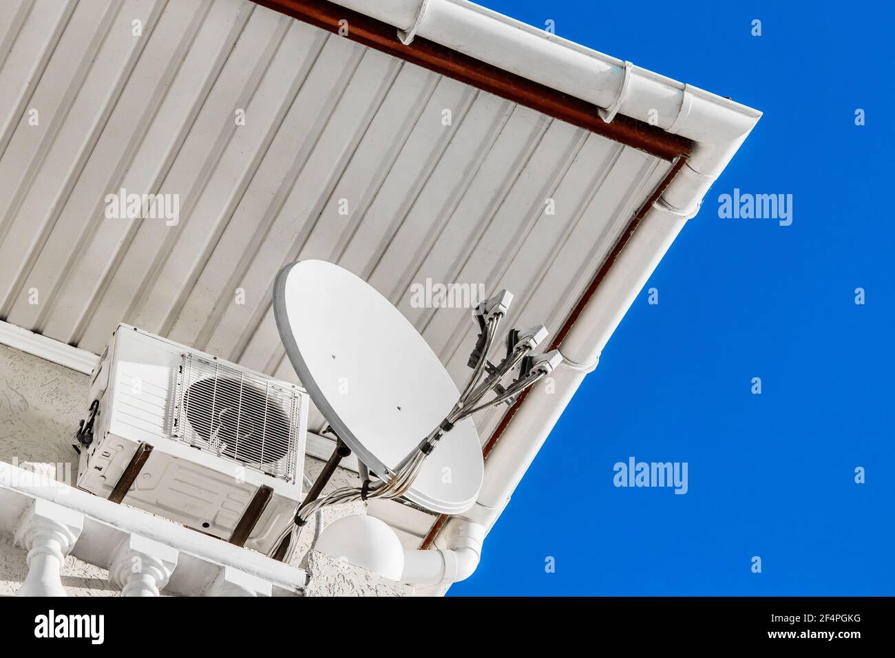 Antenna satellitare che trasmette il segnale accanto all'aria condizionata sotto il tetto dell'hotel contro il cielo blu. Foto Stock
