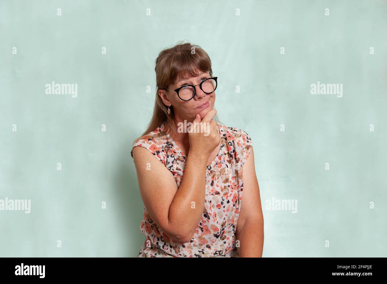 Donna caucasica bionda di media età con occhiali neri o occhiali con la mano al mento e un'espressione di pensiero sul viso. Foto Stock