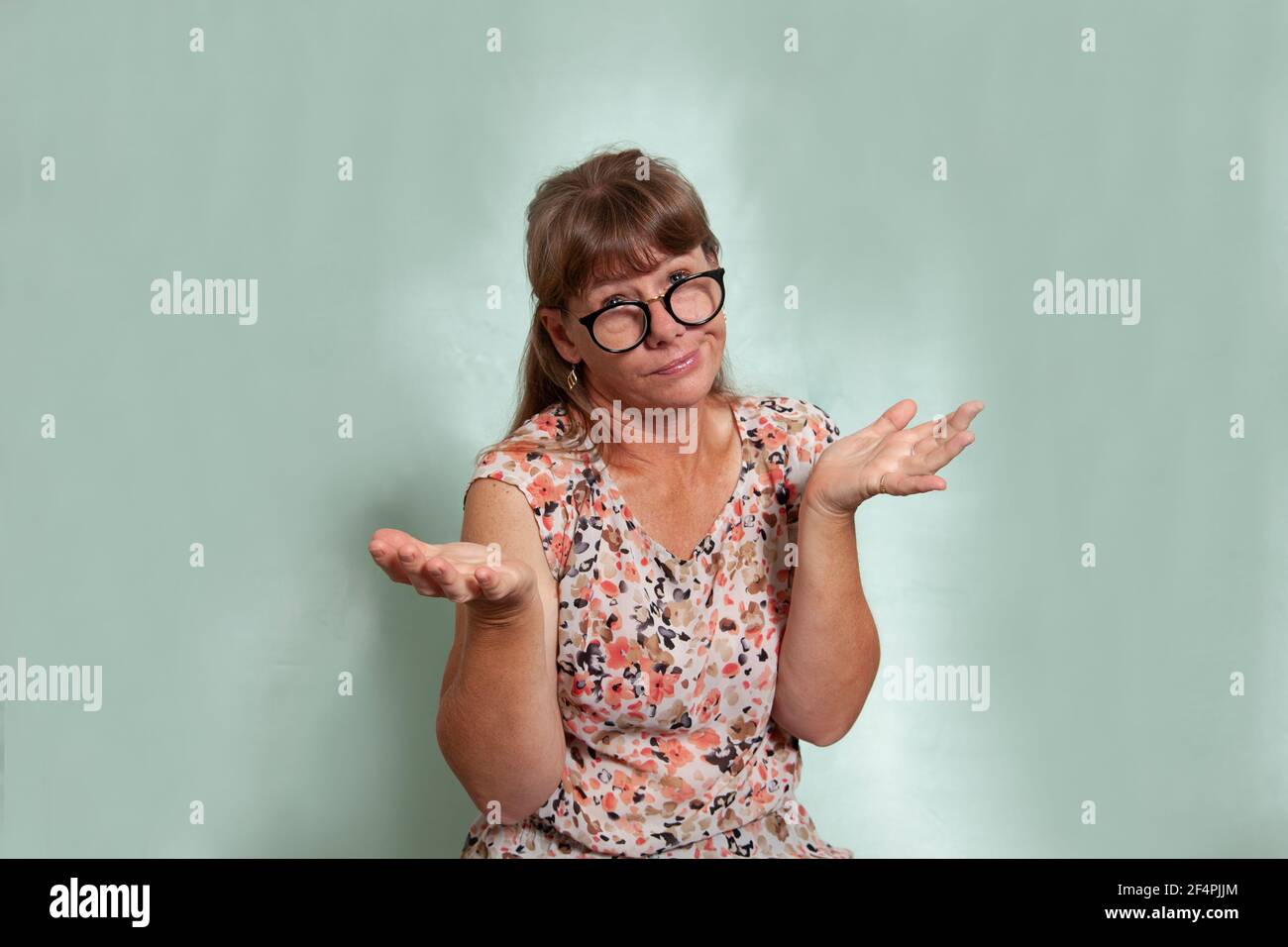 Donna caucasica di media età che guarda sopra i suoi occhiali, le sue spalle si strugge e dicendo che non sa con la sua espressione e le mani. Foto Stock