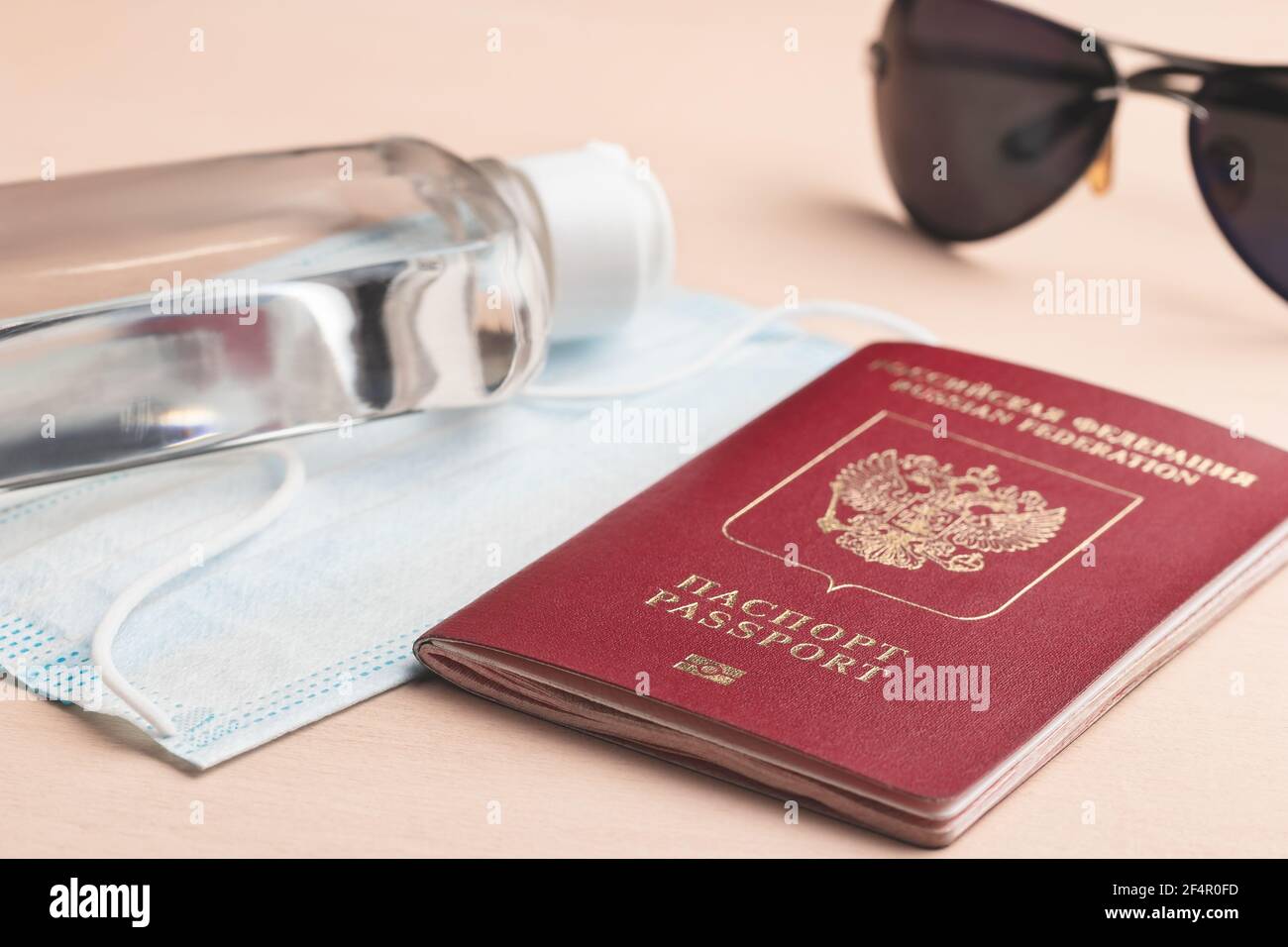 Viaggio sicuro durante il concetto di pandemia di coronavirus. Maschera medica protettiva, occhiali da sole, disinfettante e passaporto russo sul tavolo. Foto Stock