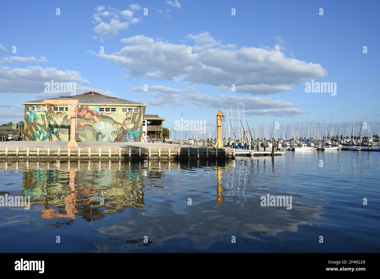 Riflesso d'acqua delle barche a vela e costruzione con murale sulla parete in una giornata nuvolosa ma soleggiata vicino al molo di San Pete. San Pietroburgo, Florida, Stati Uniti Foto Stock
