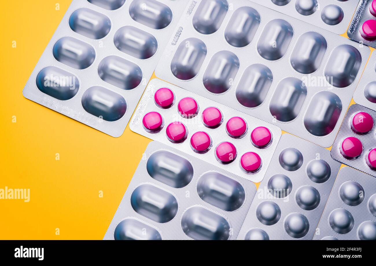 Compresse rotonde rosa compresse in blister e capsula in alluminio argento su sfondo giallo. Industria farmaceutica. Farmacia Foto Stock