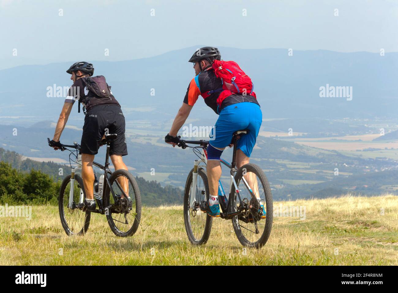 Due uomini in mountain bike vanno giù per il prato stile di vita attivo persone che vanno in bicicletta con gli amici all'aperto in bicicletta zaino Foto Stock